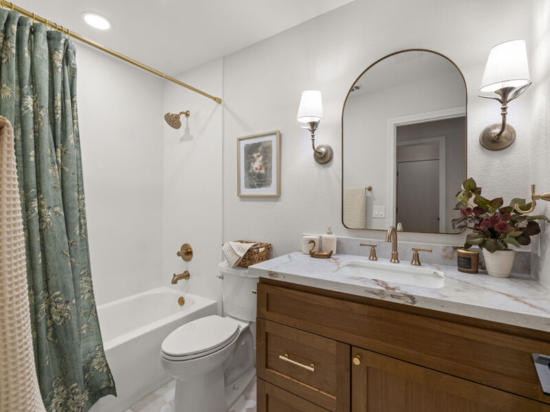 Complete bathroom remodel featuring a custom wood vanity, quartz countertop, brushed brass fixtures, bathtub, and decorative lighting.