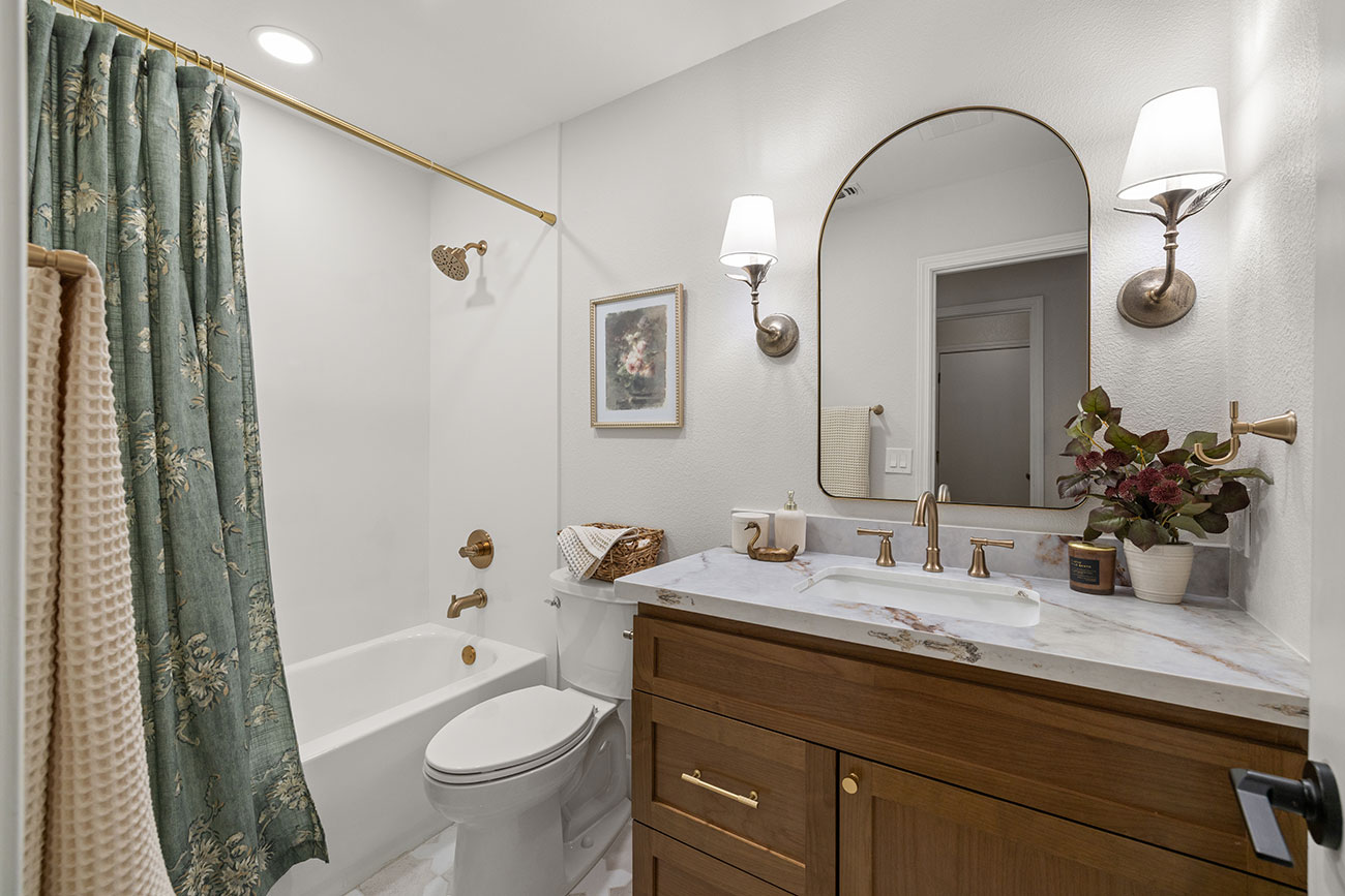 Complete bathroom remodel featuring a custom wood vanity, quartz countertop, brushed brass fixtures, bathtub, and decorative lighting.